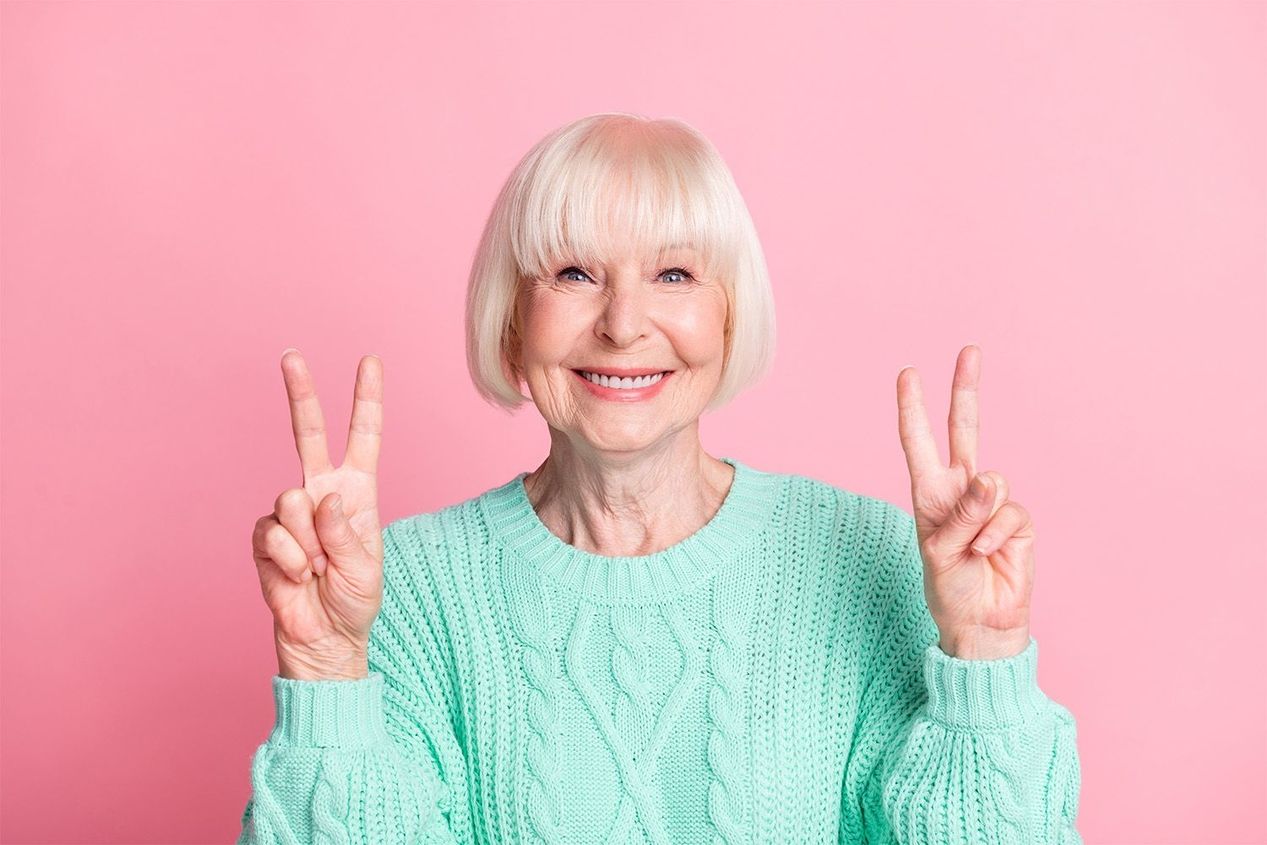 Eine Person in einem mintfarbenen Pullover macht Friedenszeichen vor einem rosa Hintergrund