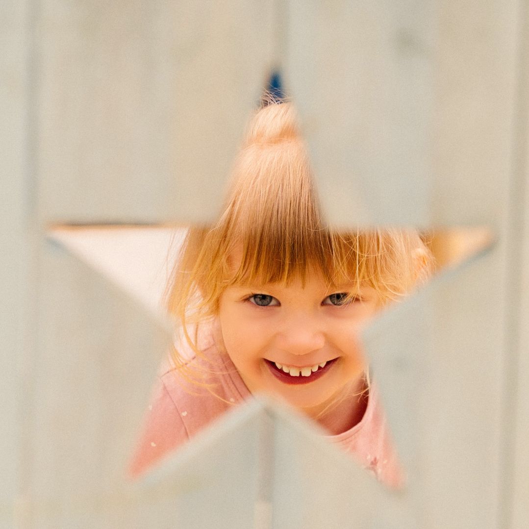 Kind mit roten Haaren, das in einer kreativen Sternform posiert, mit einem fröhlichen und lebhaften Ausdruck.